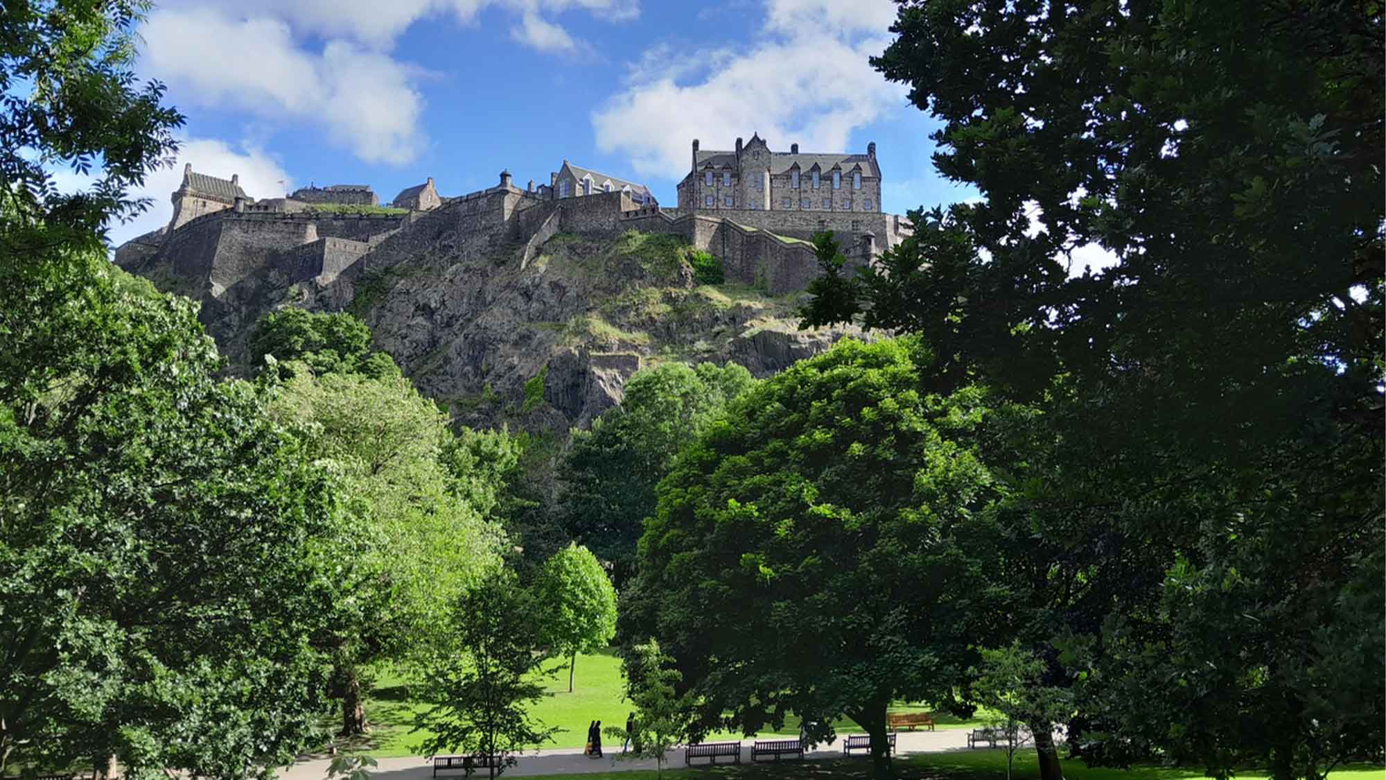 Fall trees frame the image with Edinburgh castle high above on the hill under a blue sky