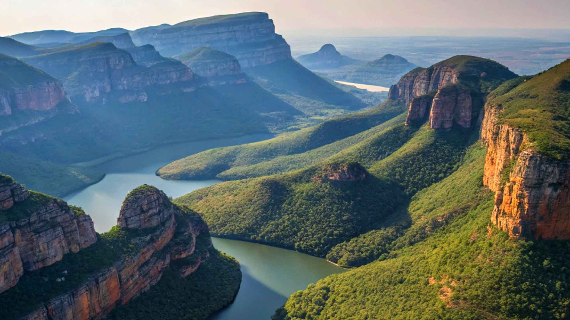 An elevated view looking out over Blyde River Canyon,  Mpumalanga. With the river curving round the lush green hills that rise up night and steep on both sides.