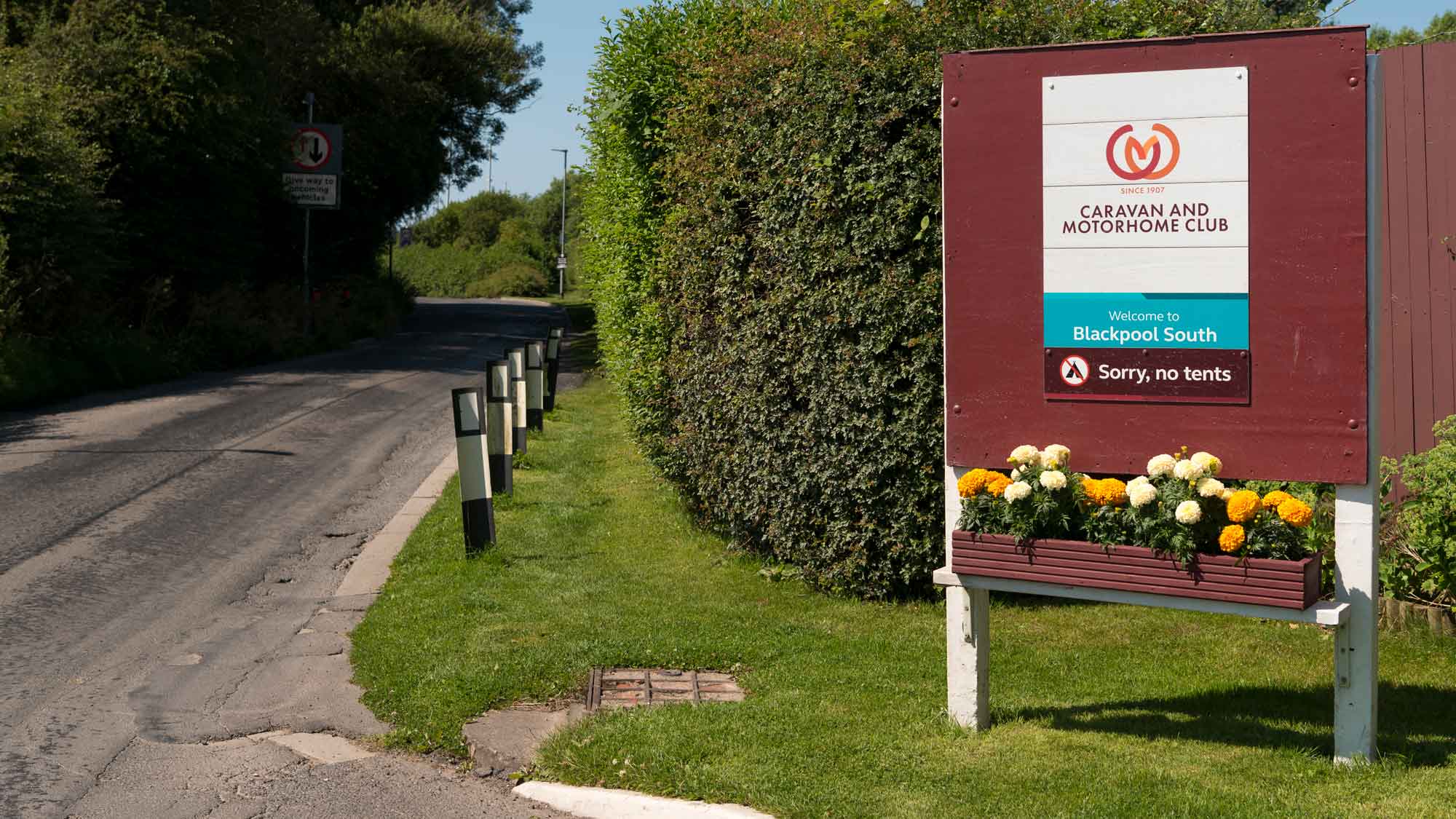 A sign beside the road for Blackpool South UK Club Campsite with flower pots full of lovely yellow flowers