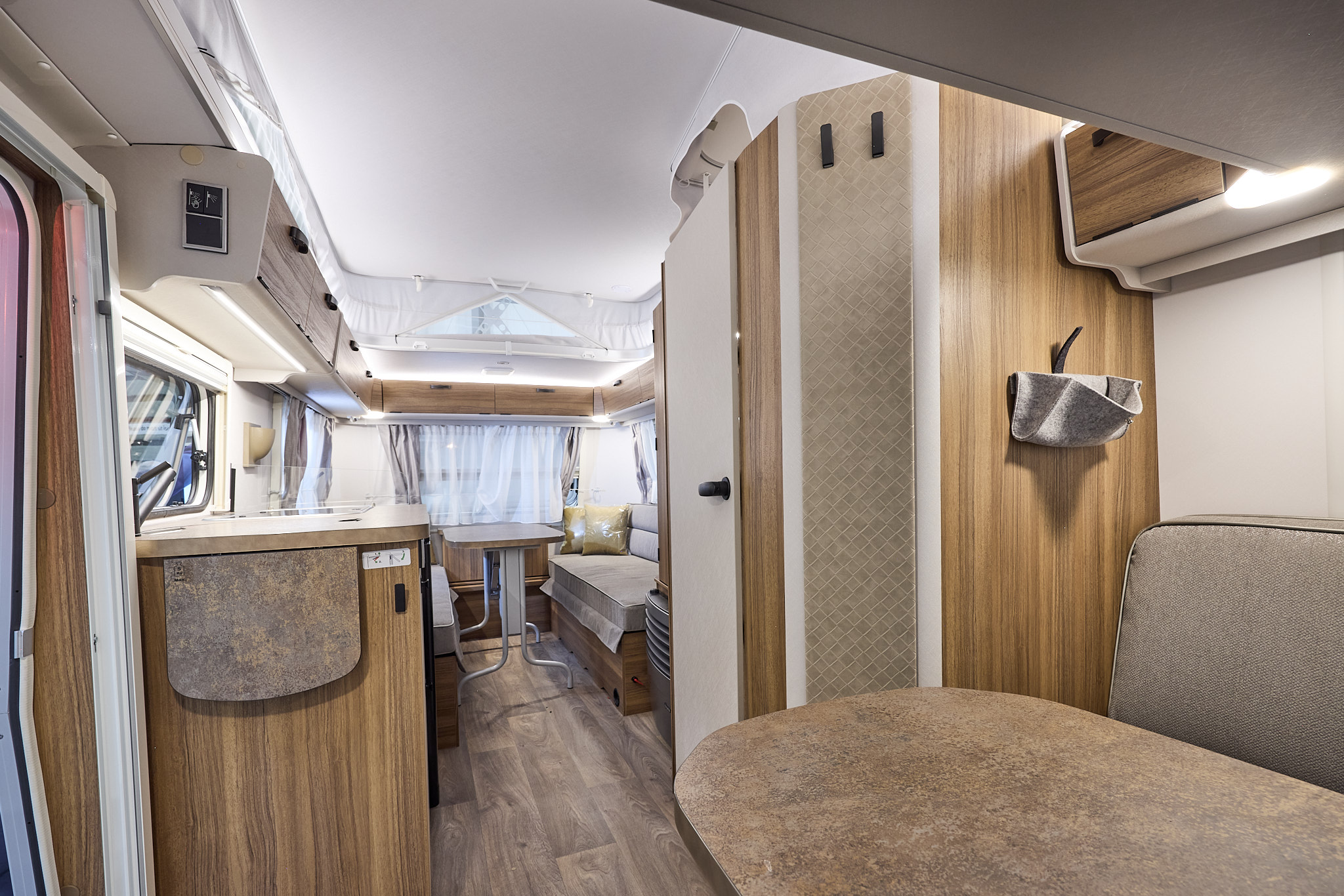 Interior of the Eriba Touring 540 Legend with grey sofas, beige accents and a wooden floor.  To the rear there are two sofas and a free standing table.