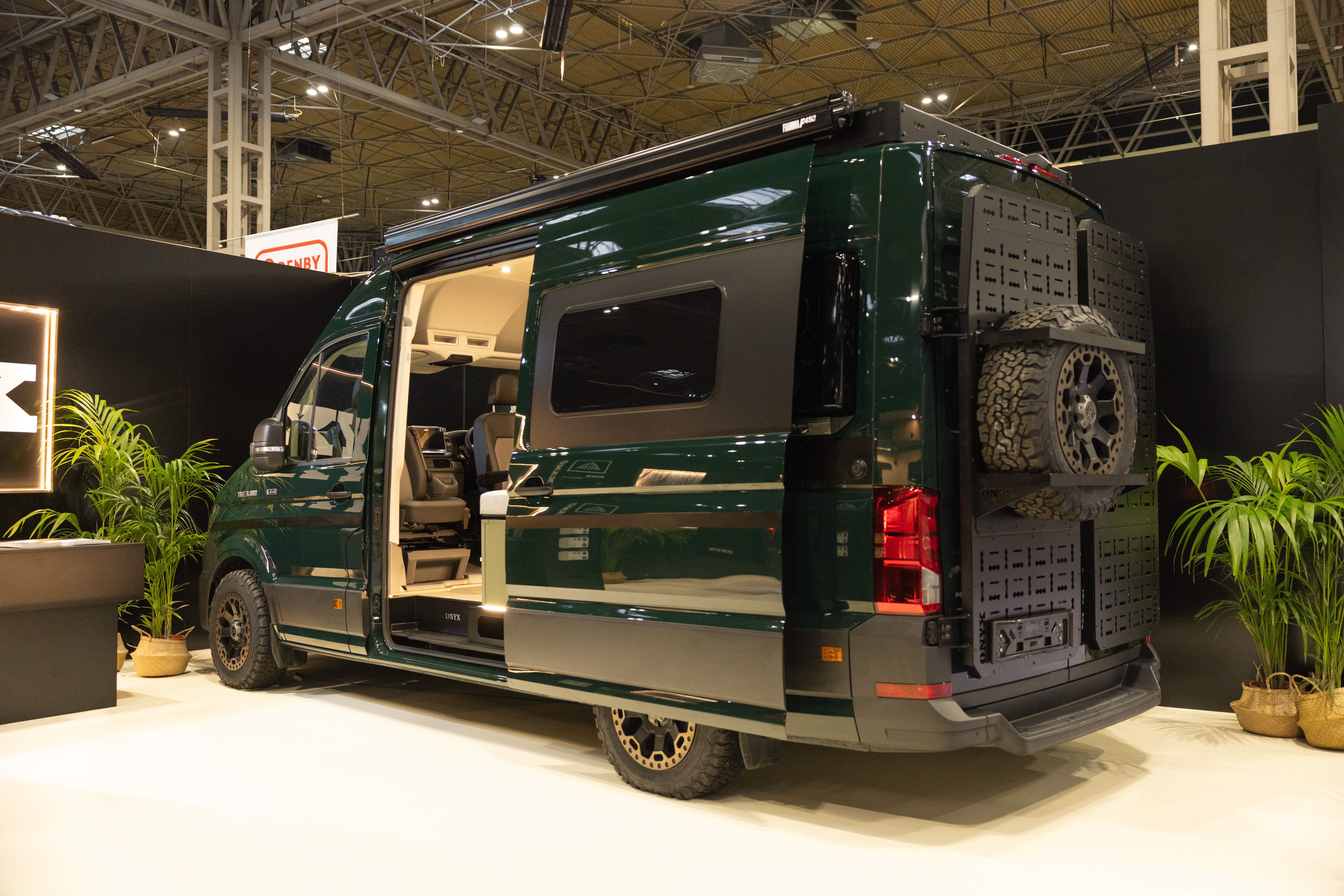 The Onyx Vans Summit 2.0 is dark green, its sliding door is open.  There is a spare wheel on the back of the vehicle.