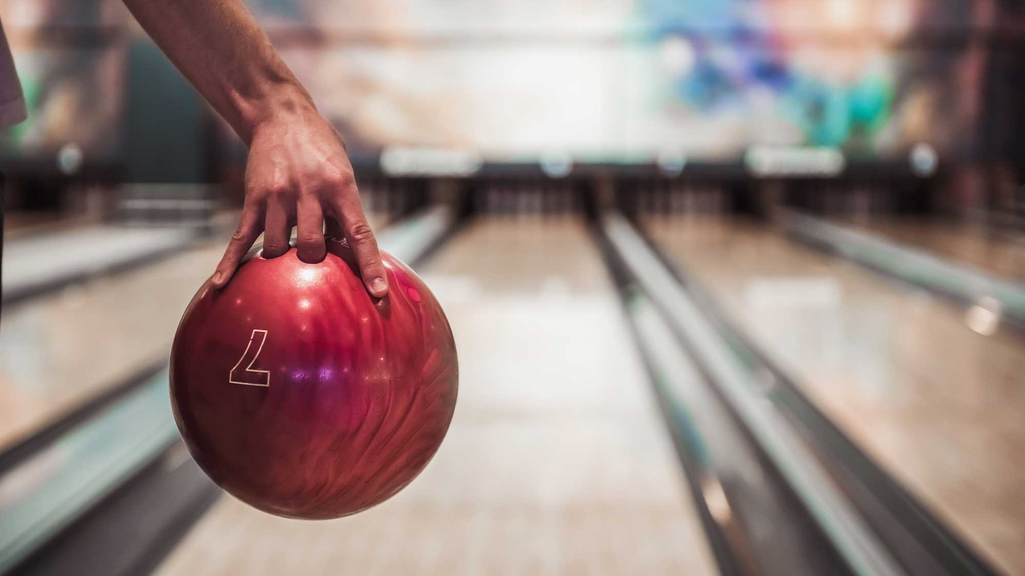 A person's hand about to roll a bowling ball at the pins at a bowling alley