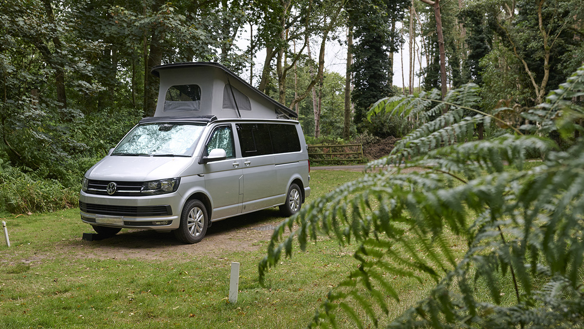 A campervan on an electric touring pitch in a leafy section of the campsite
