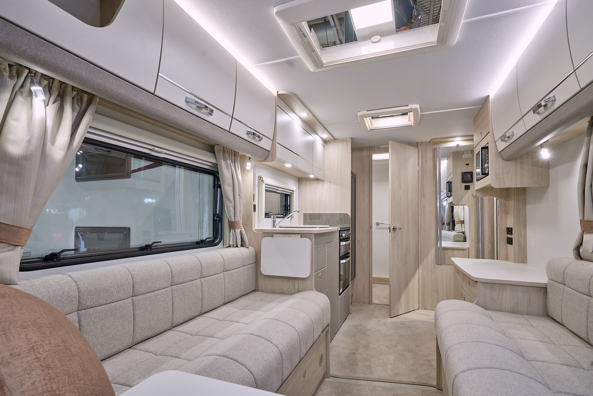 Elddis Avanté 520’s interior has cream upholstery with pale wooden furniture.  The kitchen is in the middle and the end washroom’s door is open.