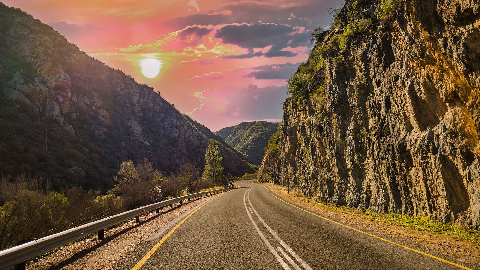 Road disappearing in the distance with high rocky cliffs with an amazing pink sky and beautiful sunset at Western Cape South Africa.