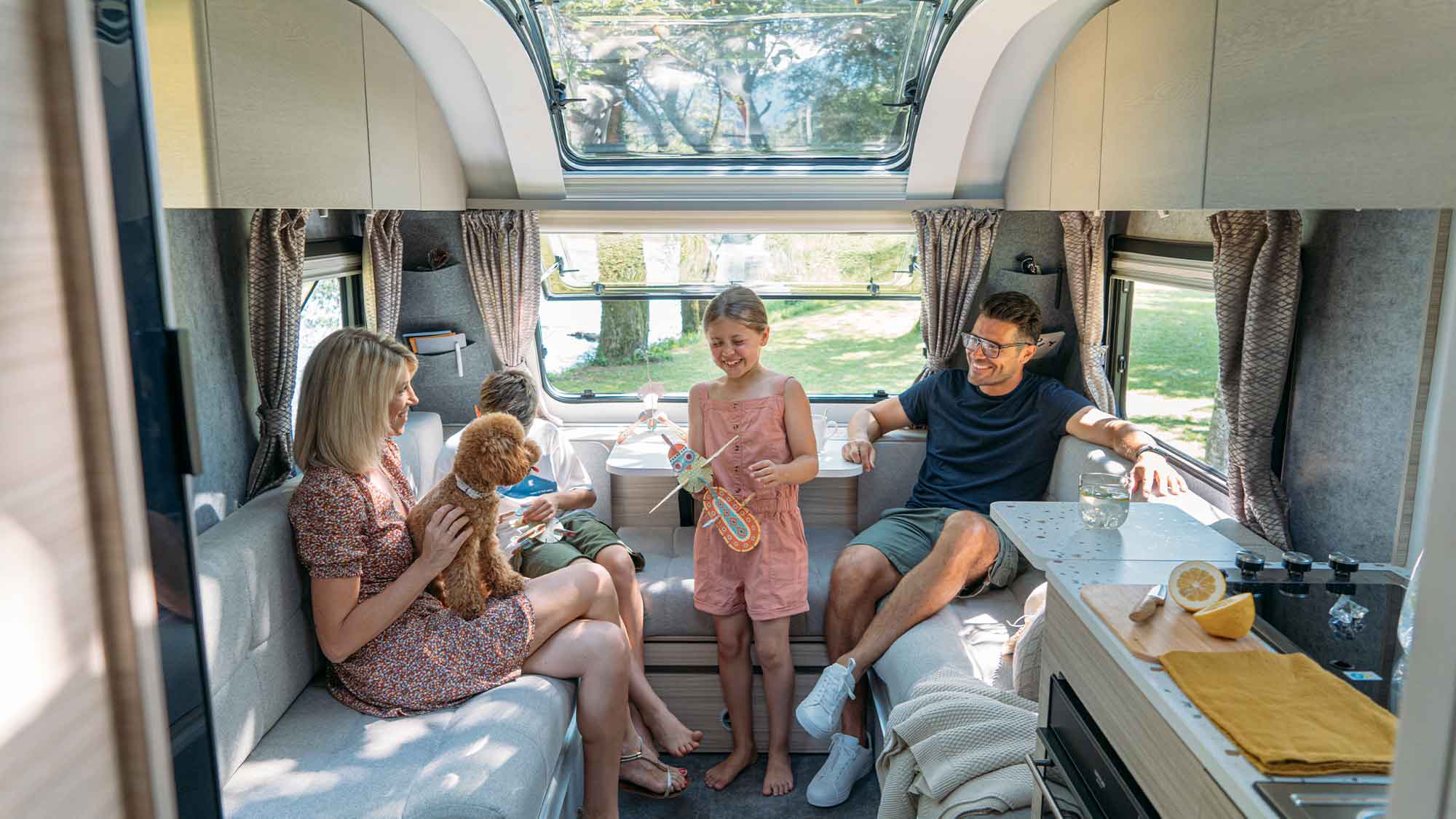 Inside an Adria Altea caravan with a smiling family sitting with a dog
