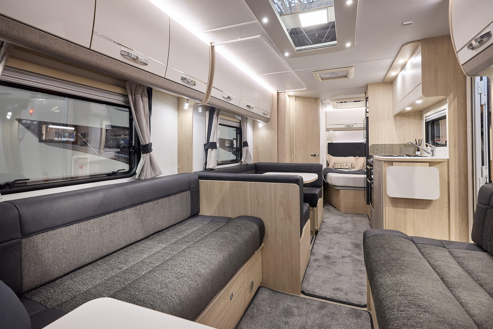 Interior of the Elddis Avanté APEX 840 with dark grey sofas, wood accents and grey carpets.  The large roof light will let natural light flood in.  There is a dinette opposite the kitchen.