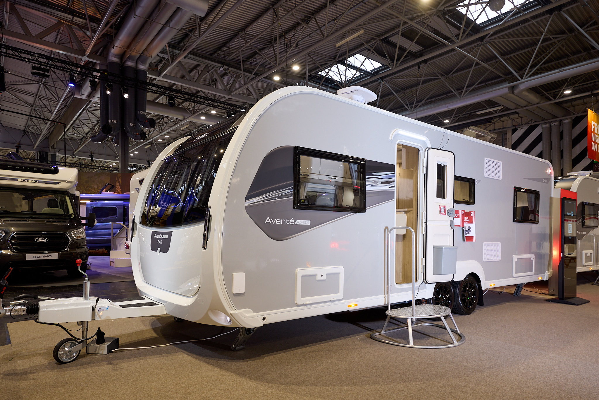 The Elddis Avanté APEX 840 has a grey exterior with a grey and black decal.  The entrance door is open and there is a metal step to gain easy access.