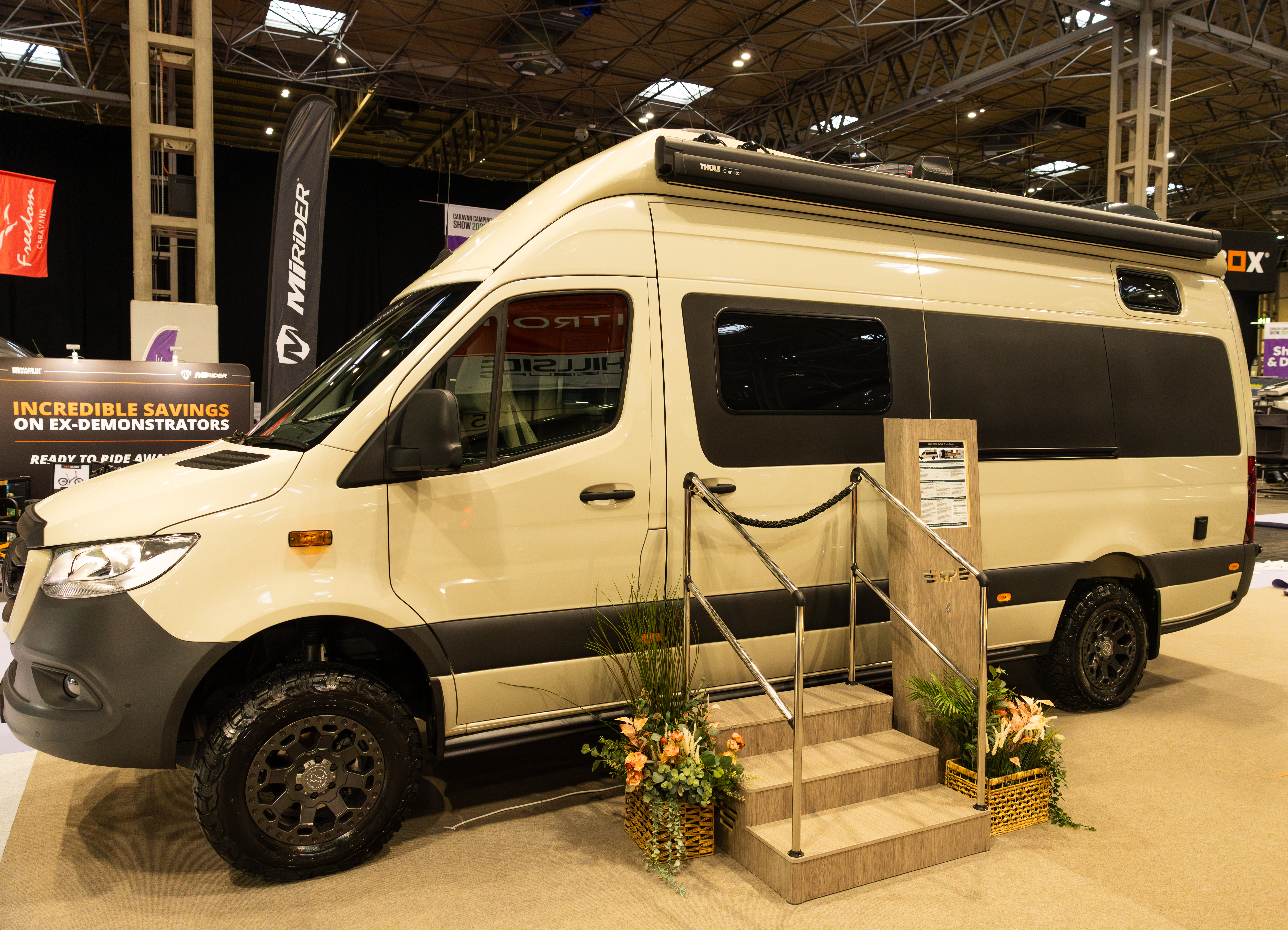 The RP Motorhomes Rebellion 2 is cream.  There are three steps with rails to gain easy access.  Next to the steps are two flower arrangements and there is an information board too. 