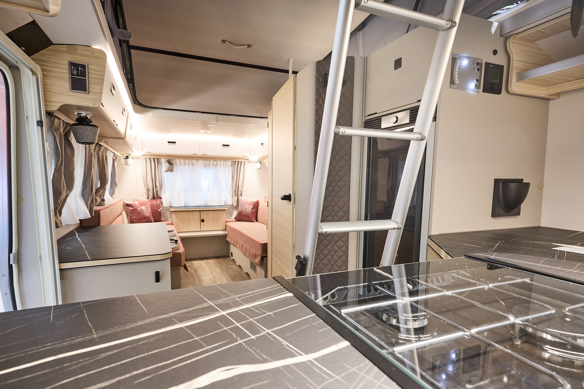 Interior of the Eriba Touring 620 Tango Red Edition with pink sofas, cosy red cushions, wooden accents and a wooden floor.  To the front is the kitchen and there’s a ladder to gain easy access to the pop top roof.