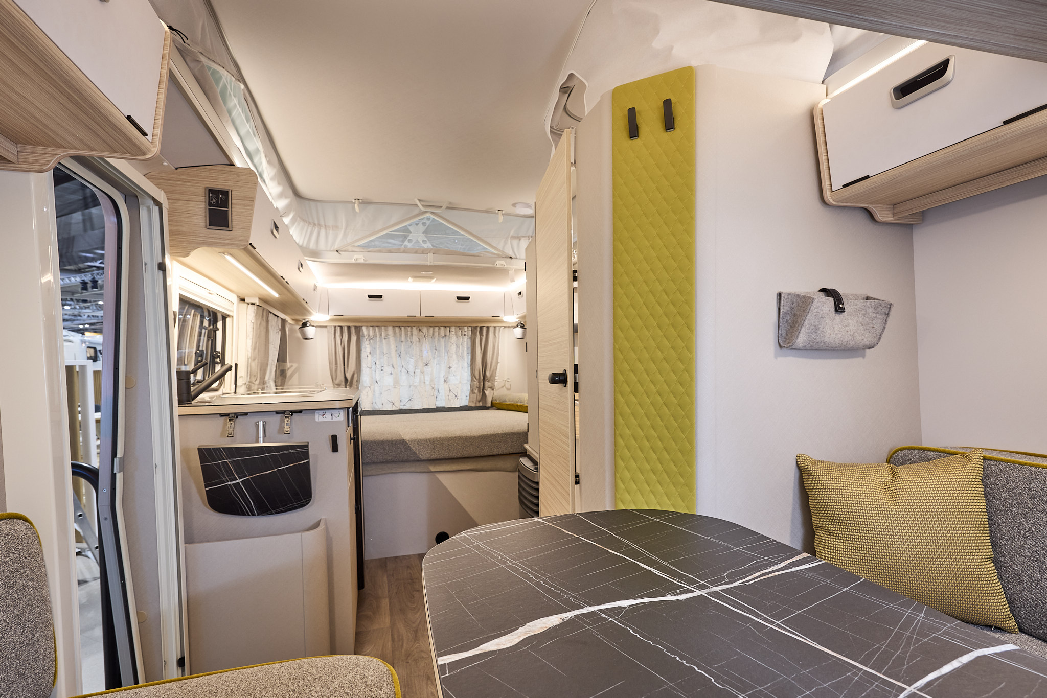 Interior of the Eriba Touring 530 Urban with grey sofas, lime green accents and a wooden floor.  To the rear there is a large fixed bed.