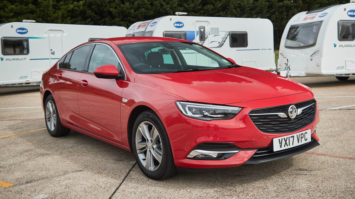 Red Vauxhall parked in front of three white caravans