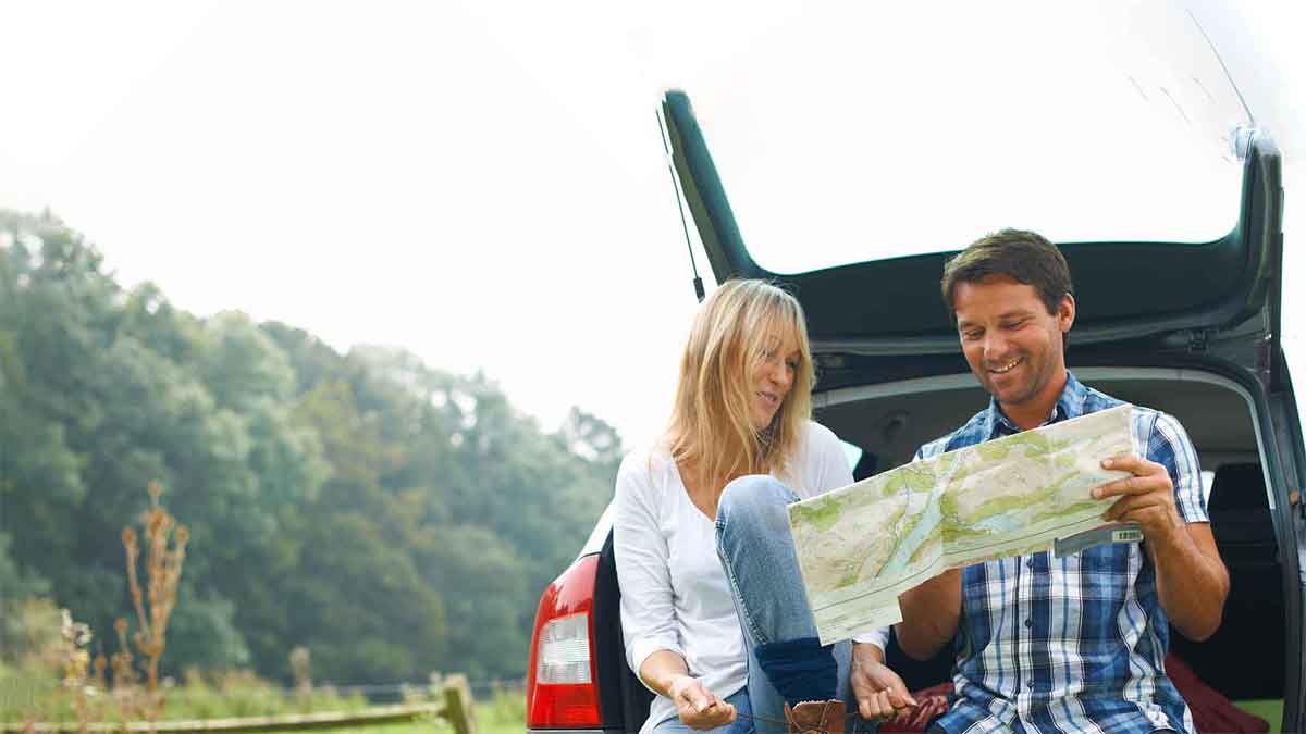 Man and woman perched on the back of their car looking at a map
