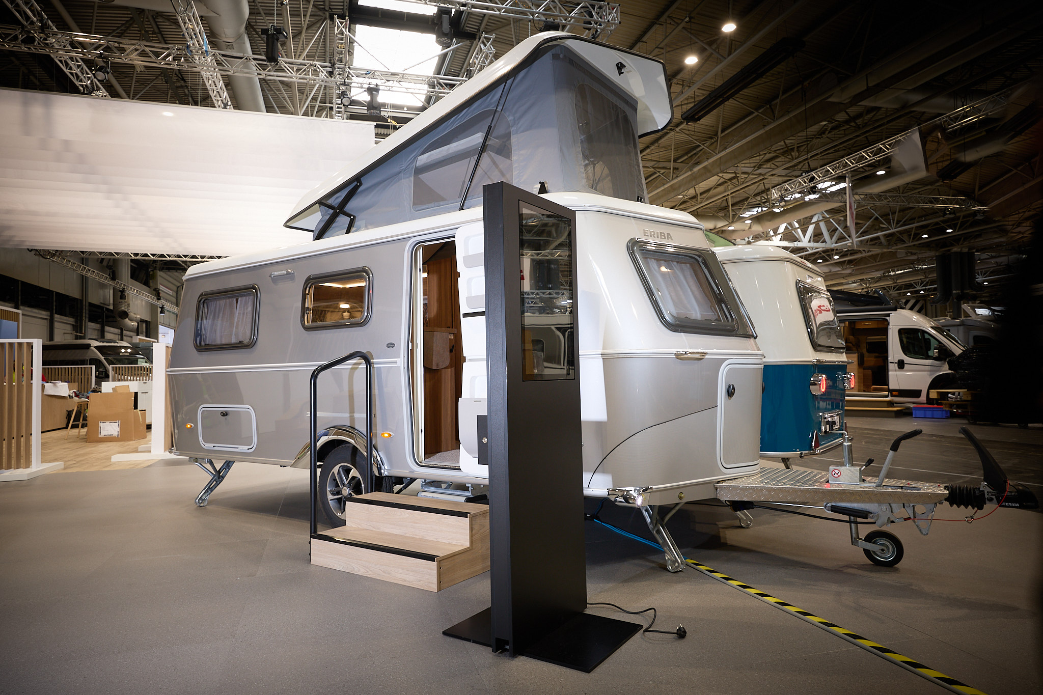 Eriba Touring 642 Legend exterior is silver with a white panel at the front.  The large pop top roof is open.  There are two wooden steps to to the interior.