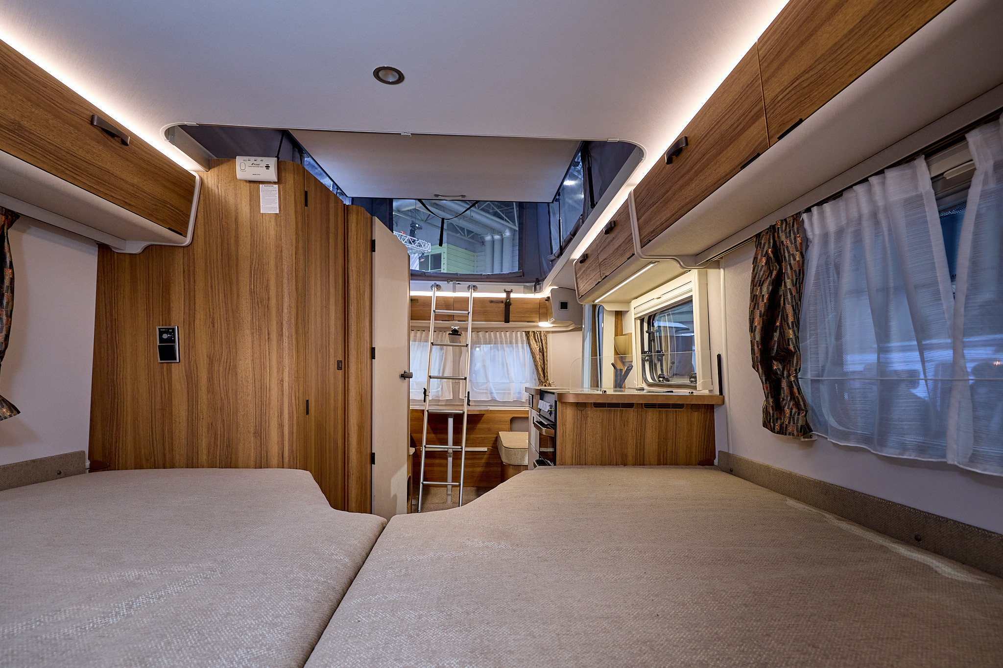 Eriba Touring 642 Legend's interior has wooden furniture with grey upholstery.  The fixed bed is at the front of the photograph.  The pop top roof is open with a ladder for easy access.