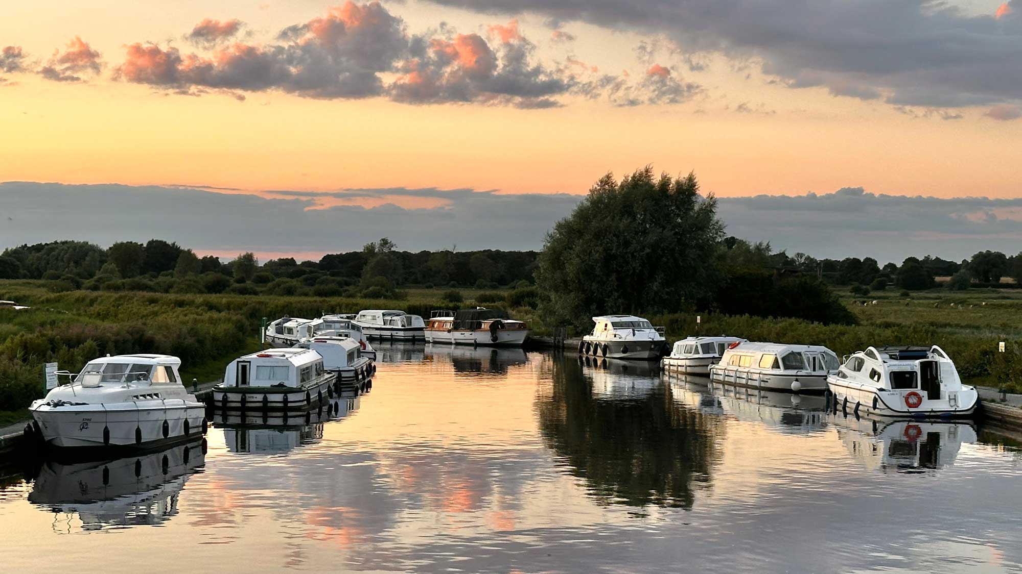 Sunset from Ludham Bridge on the Norfolk Broads with small boats moored up either side