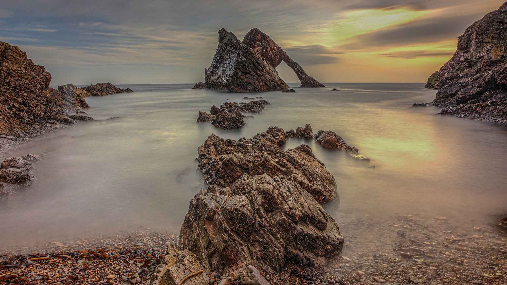 The peaks of Bow Fiddle Rock rising out in the distance with what looks like mist surrounding the rocky formations in the foreground
