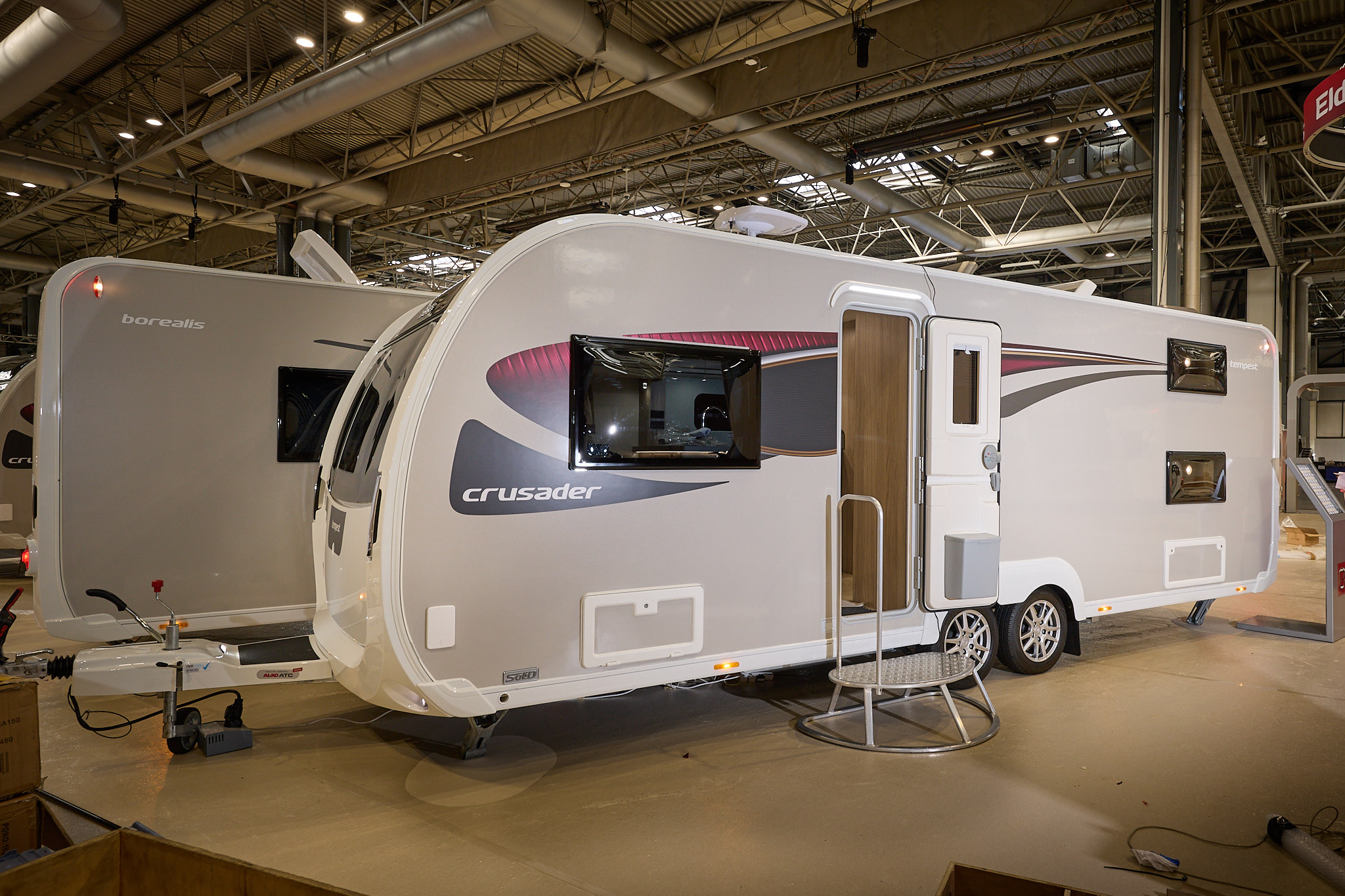 Elddis Crusader Tempest exterior is grey and white with black and red decals.  The door is open and there is a metal step to gain easy access to the interior.