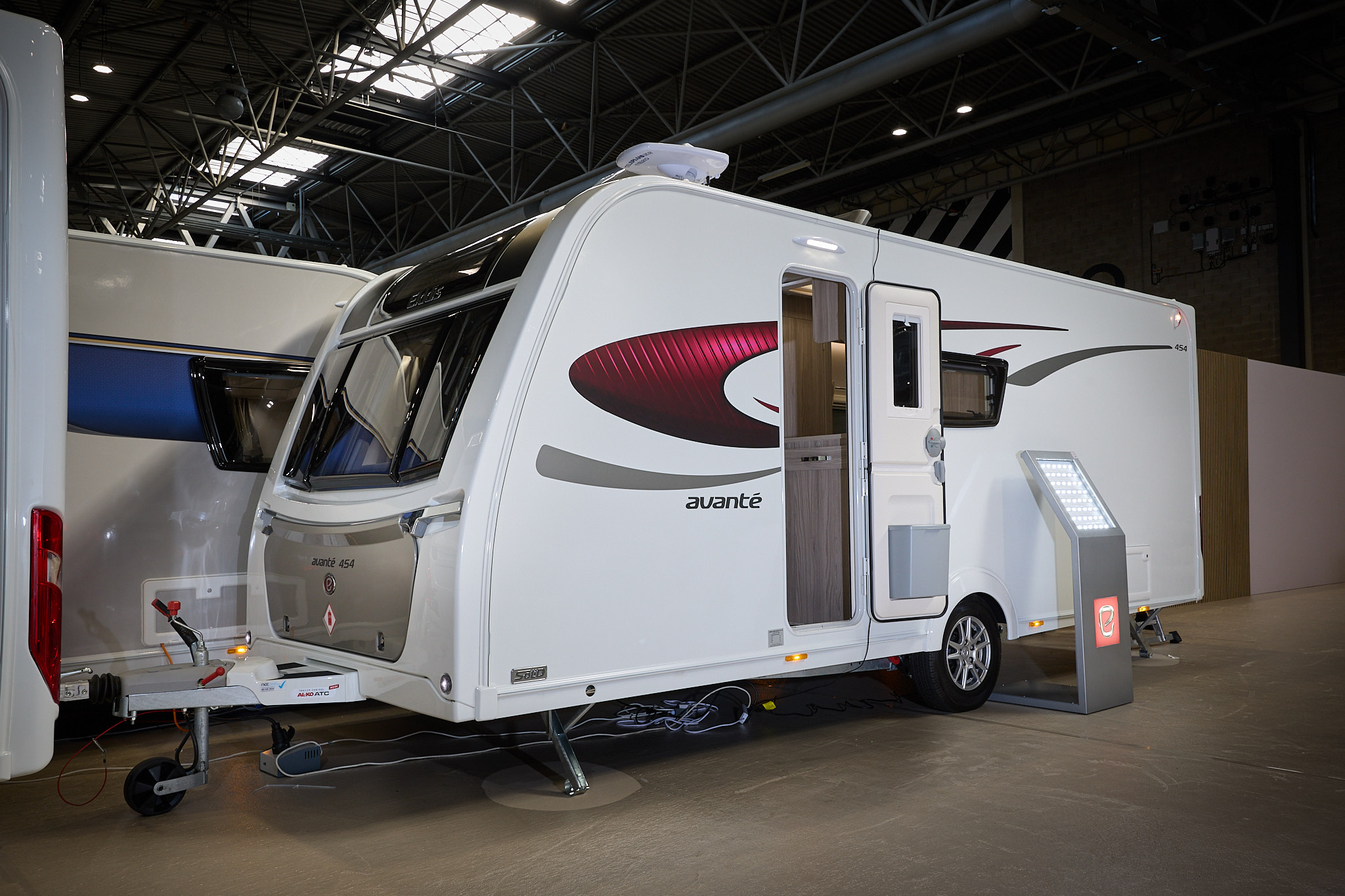 Elddis Avante 454 exterior is white with black and red decals.  There is an interactive display stand leaning against the caravan.