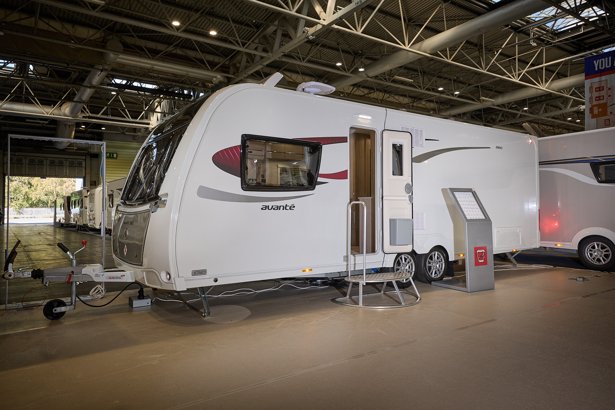 Elddis Avante 860 exterior is grey and white with black and red decals.  The door is open and there is a metal step to gain easy access to the interior.