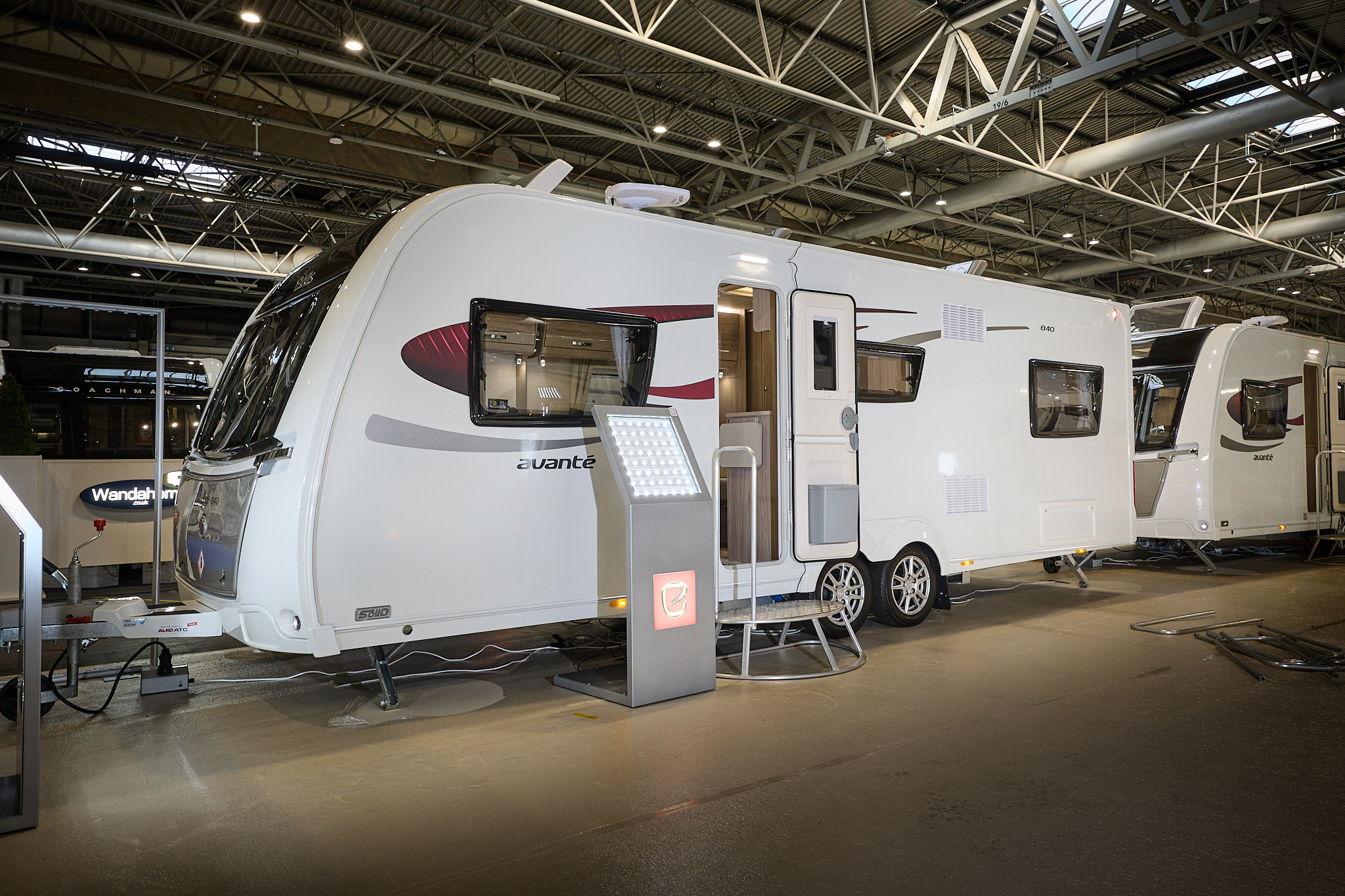 Elddis Avante 840 exterior is grey and white with black and red decals.  The door is open and there is a metal step to gain easy access to the interior.