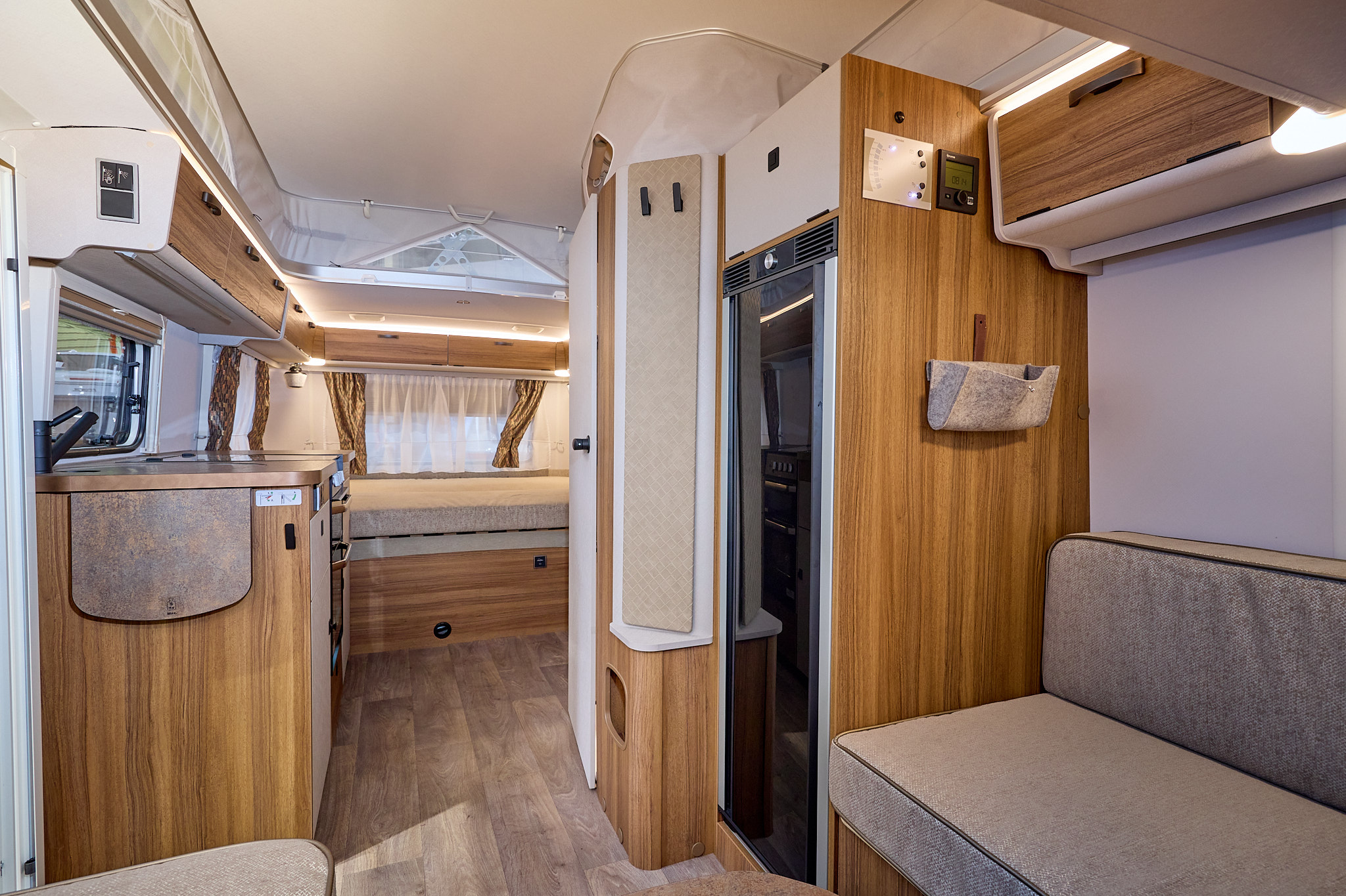 Eriba Touring 630 Legend interior is cream with wooden furniture, the front lounge has grey upholstery and there is a fixed bed at the rear.  The pop top roof is open.