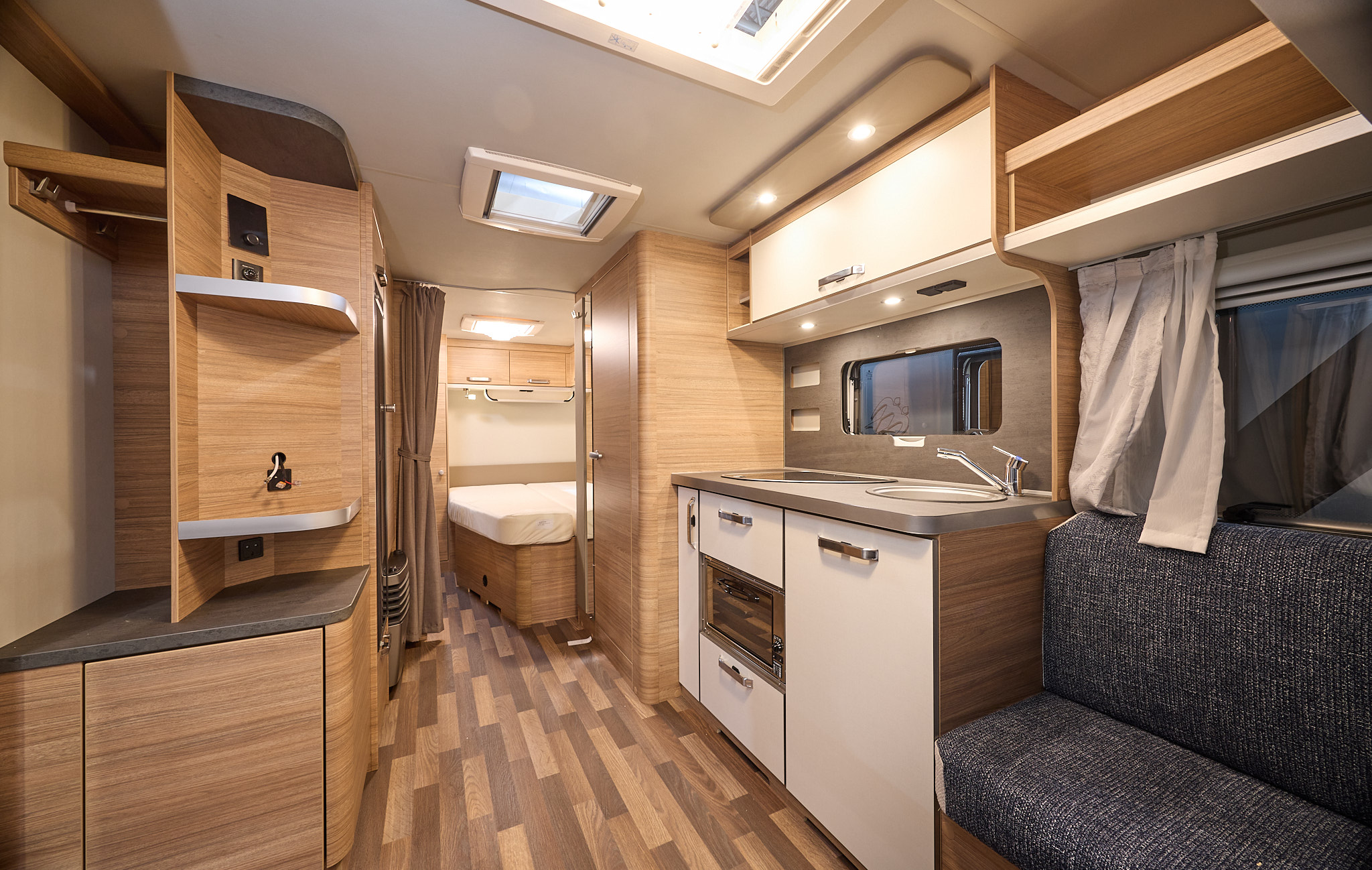 Weinsberg CaraOne 550 UK's interior is primarily wooden with dark grey upholstery.  There is a fixed bed at the rear.  The flooring is two tone wood.