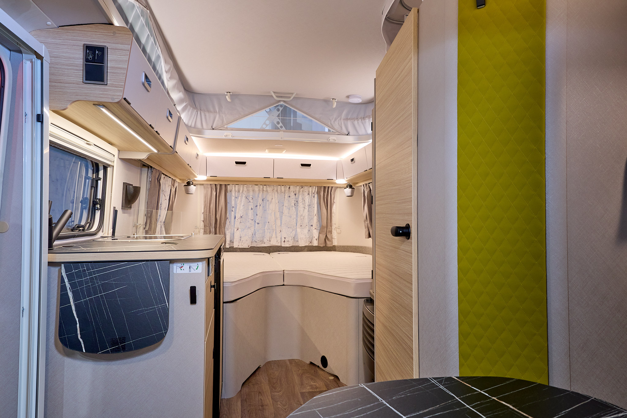 Eriba Touring 542 Urban Nugget Gold interior, it is white and cream with a yellow vertical panel.  There is a dinette at the front.  The fixed bed is beyond the kitchen.  