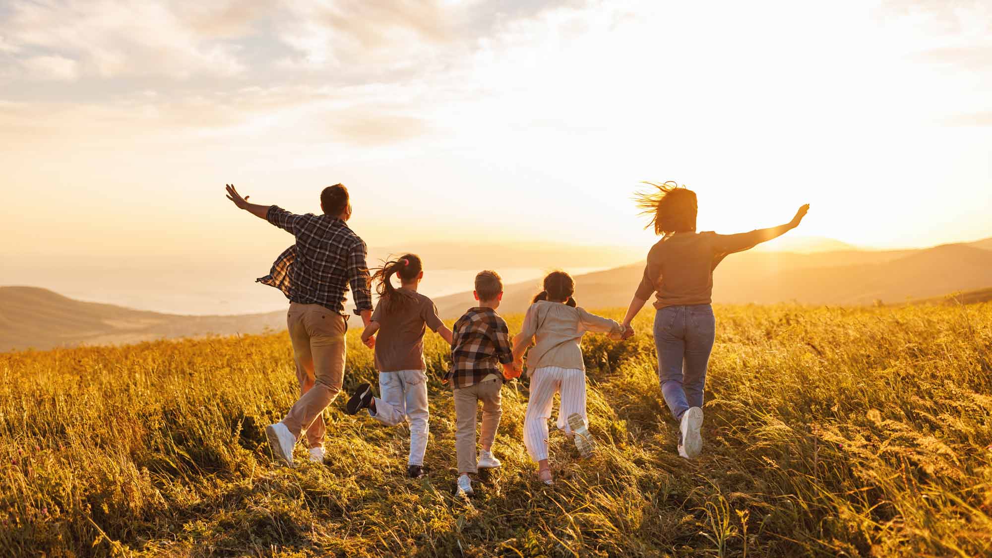 Family running across a hillside at sunset