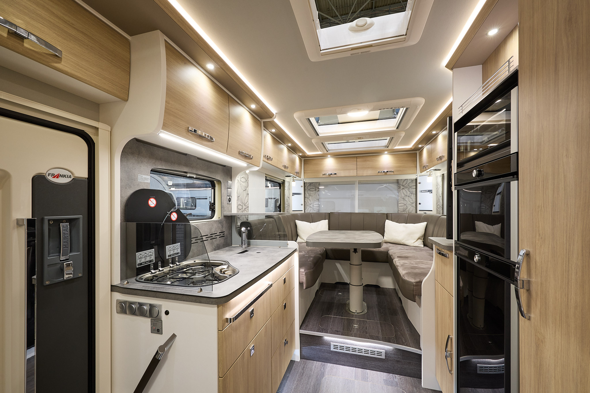 Frankia I 7400 PLUS Platin Pure Edition’s interior has wooden furniture with white surrounds.  There are three skylights.  The kitchen is central with the hob on the left and the fridge freezer on the right.  There is a u-shaped lounge to the rear.
