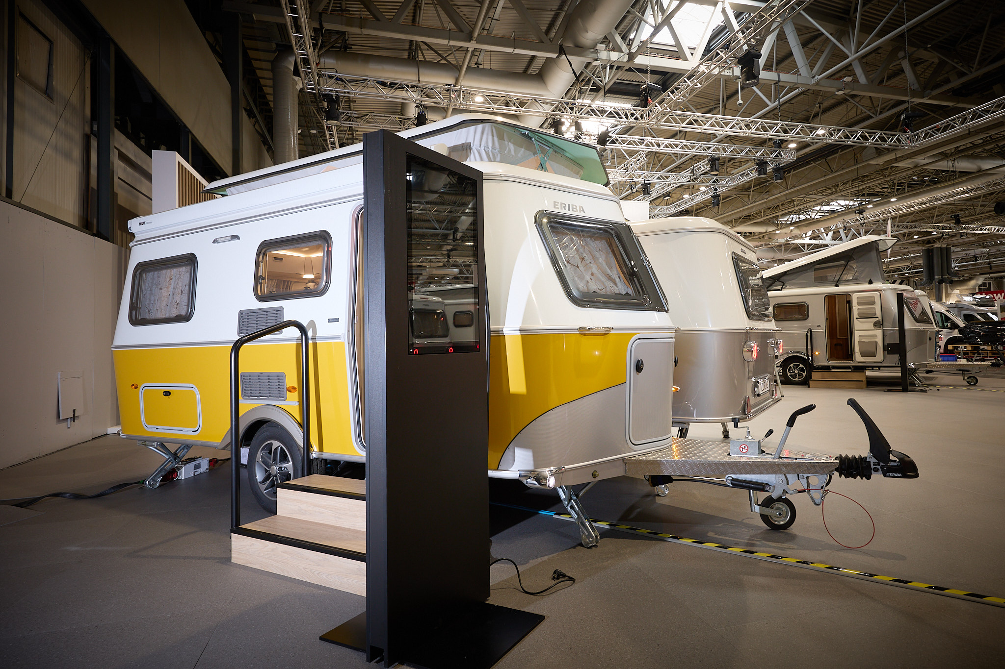 Eriba Touring 542 Urban Nugget Gold's exterior is white and yellow.  The pop top roof is open.  There are two wooden steps into the interior.