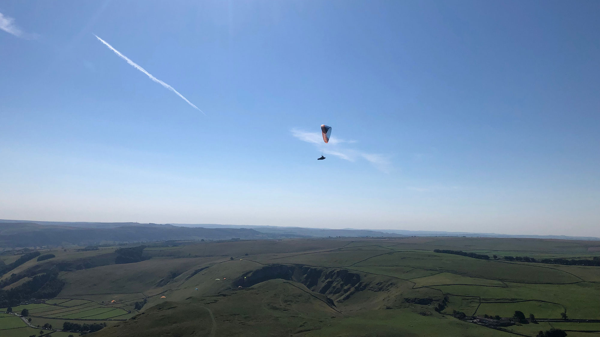 A solo paraglider floating in clear skies over the Peak District