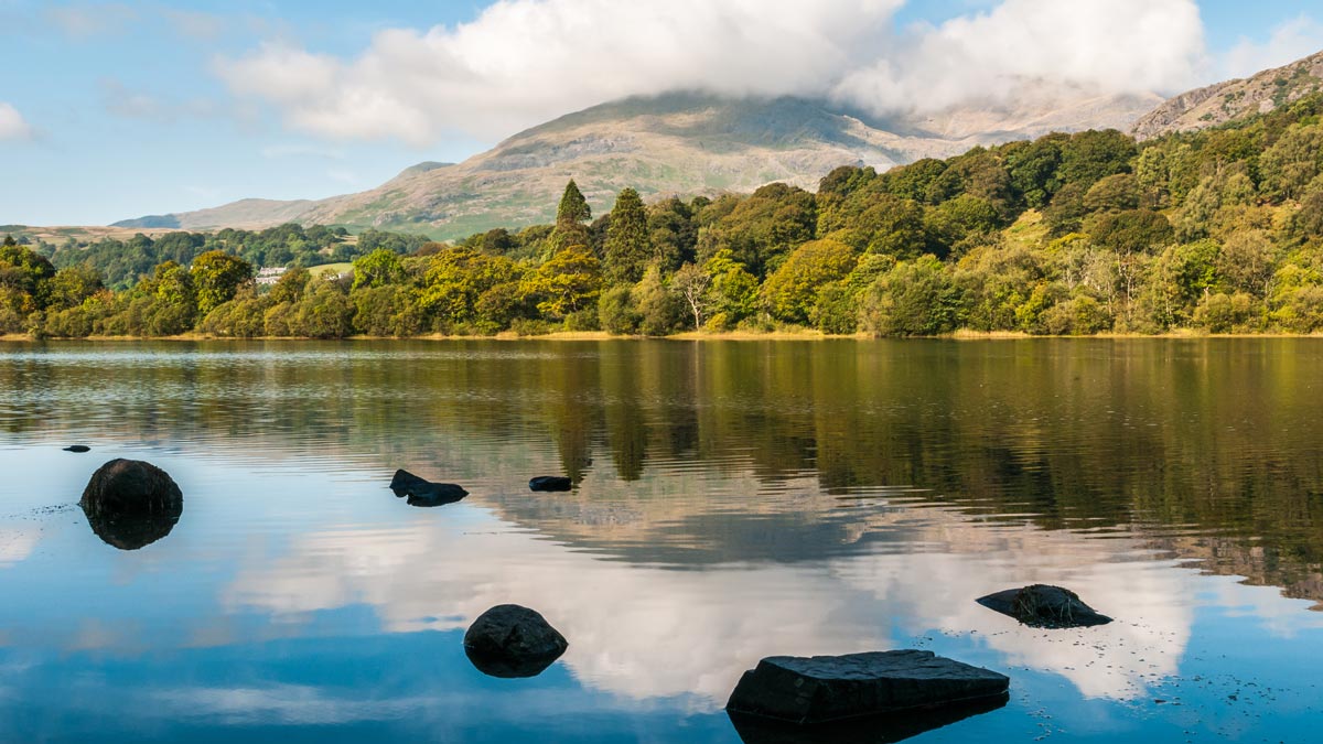 Coniston Old Man wrapped in cloud over the calm surface of Coniston Water