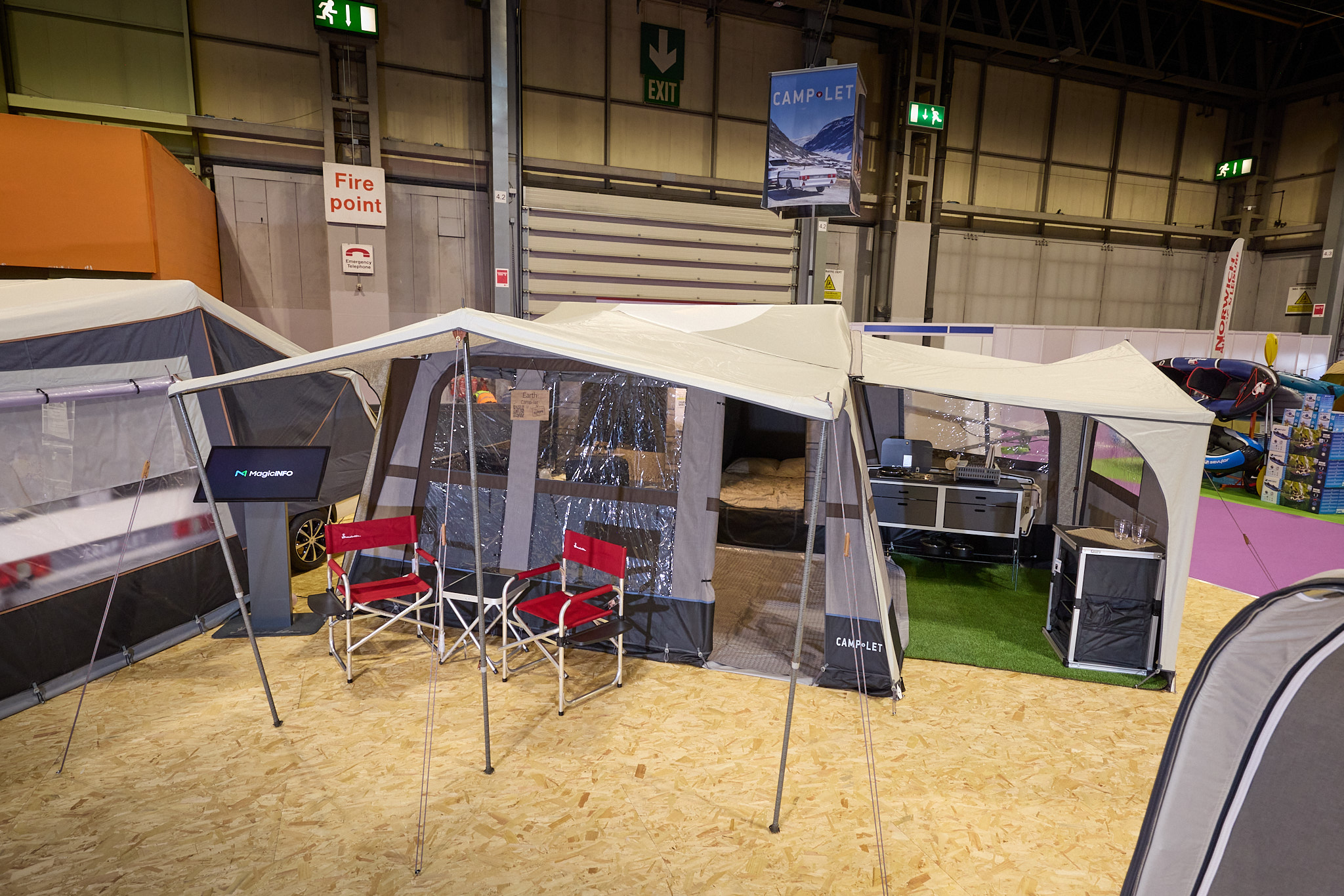 The Camp-Let Earth has a cream canvas roof.  It has a separate annex for the kitchen.  There are two red camping chairs under the canopy.  The doors are open revealing the bedroom and kitchen units.