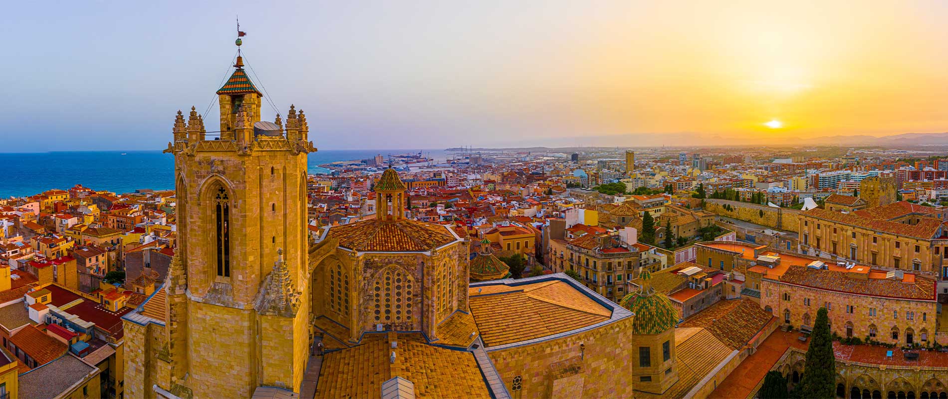 An aerial of Primatial Cathedral of Tarragona and the sandy-coloured buildings under a beautiful sunset sky in Catalonia, Spain. This is the final destination on our suggested route from Calais