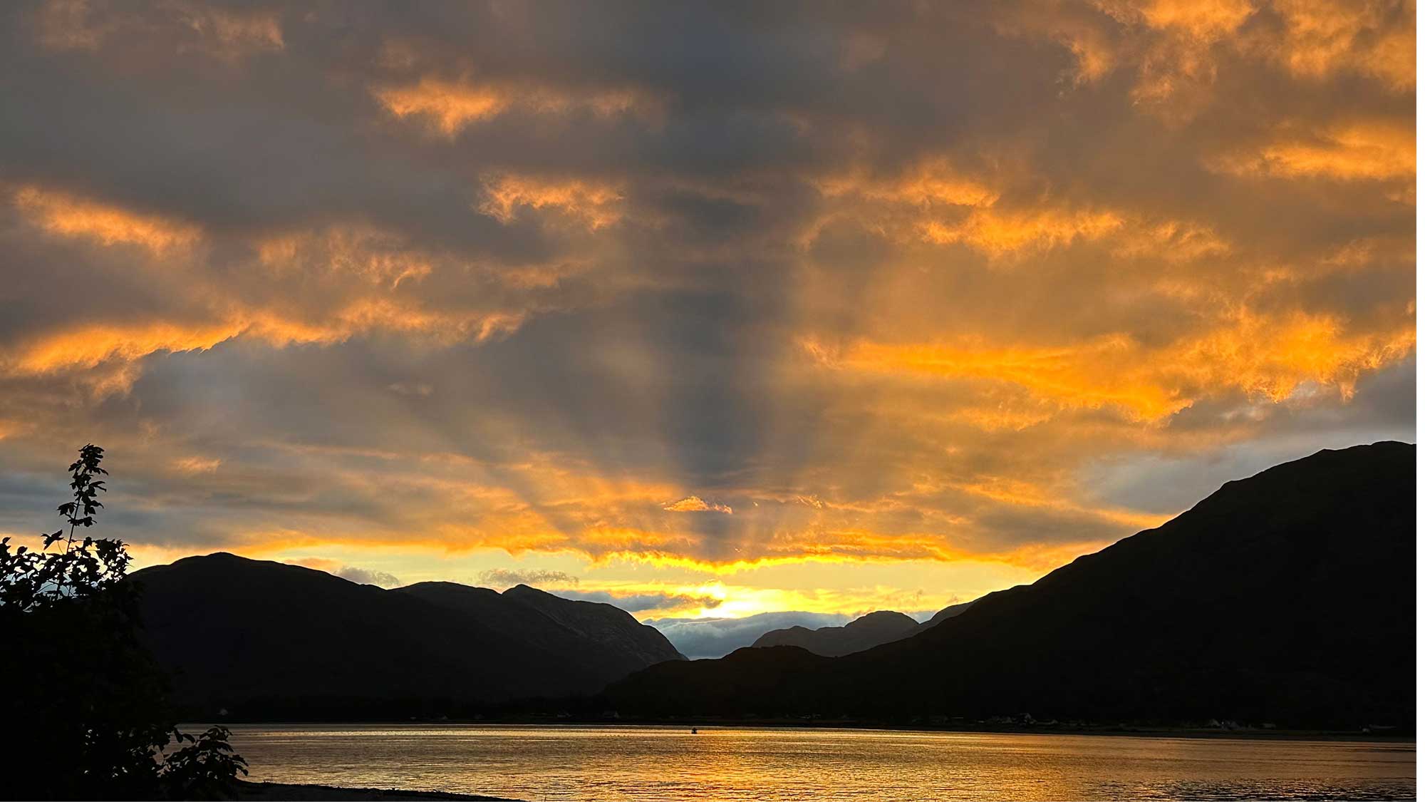 A beautiful orange sunset behind the hills in the distance with the calm waters in the foreground