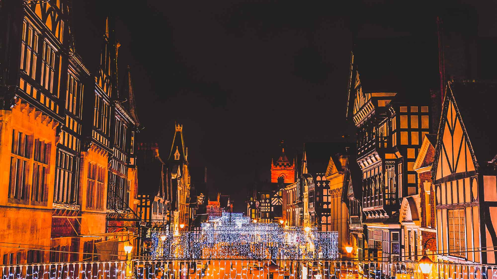 A view down the street in Chester with black and white buildings lining the street on either side with festive lights all done the street under a night sky
