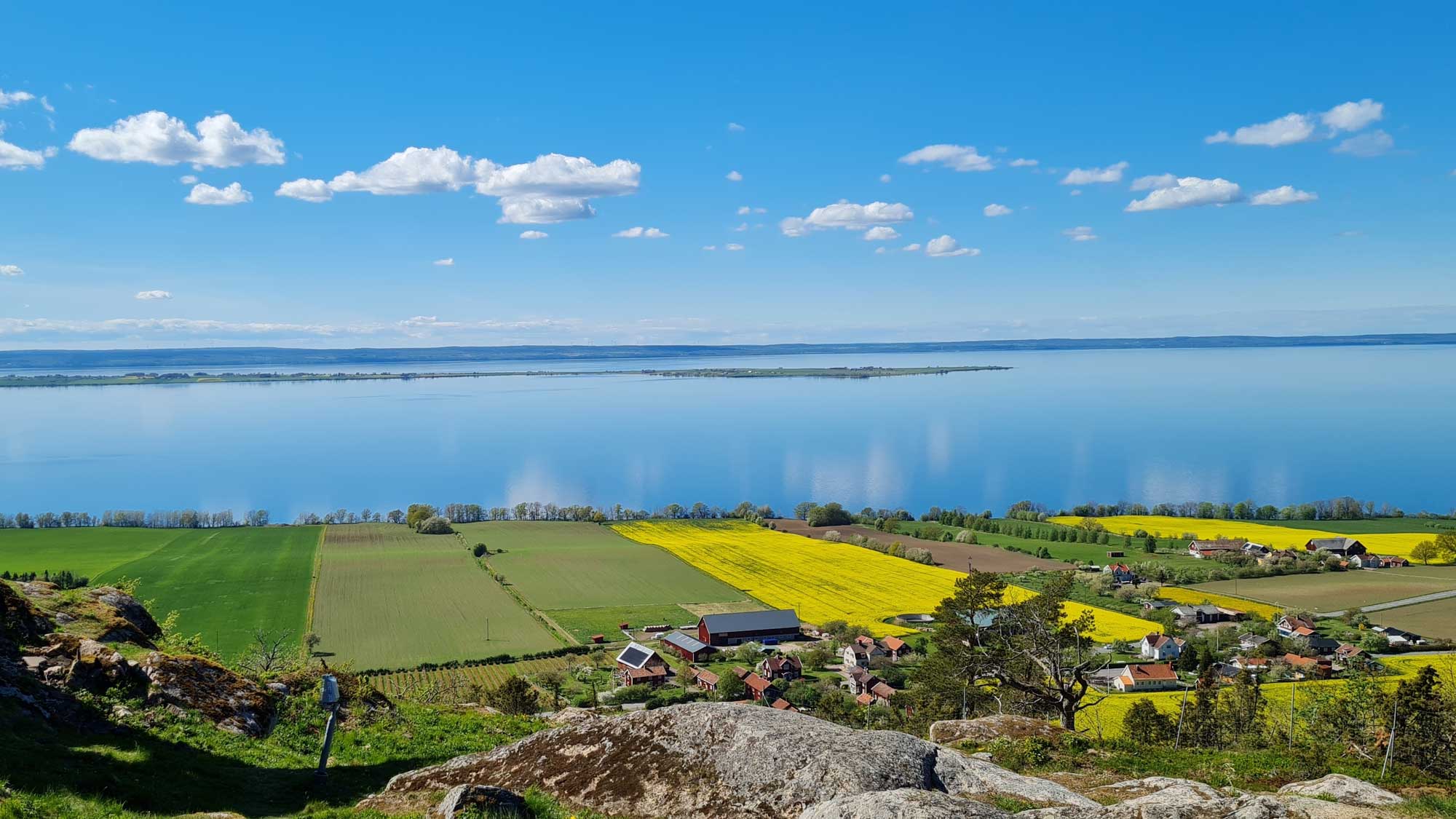 View of Lake Vättern in Sweden in summer with sky reflected in the calm water next to green fields