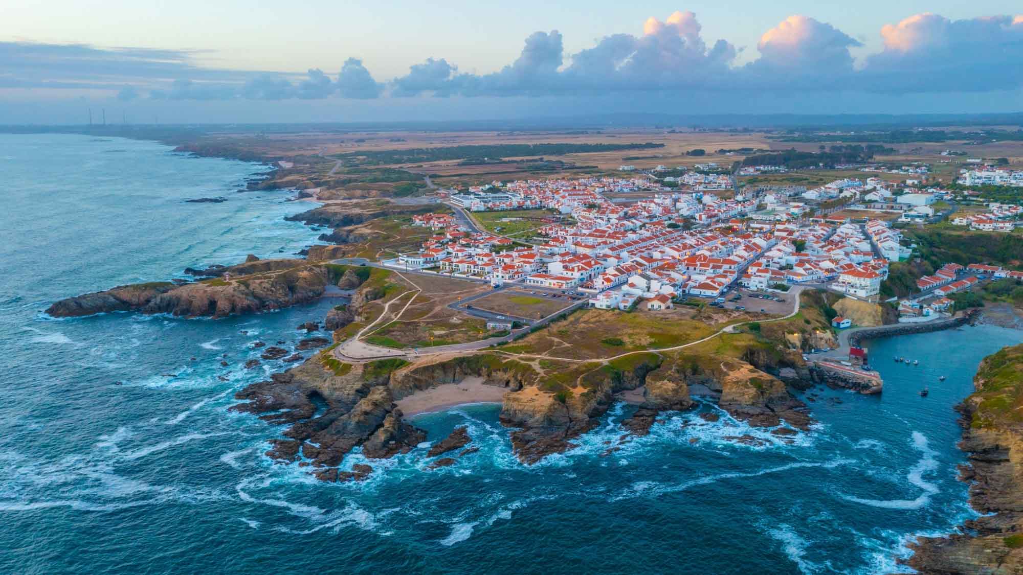 A view from above the sea looking back over the rugged coastline and buildings or Porto Covo
