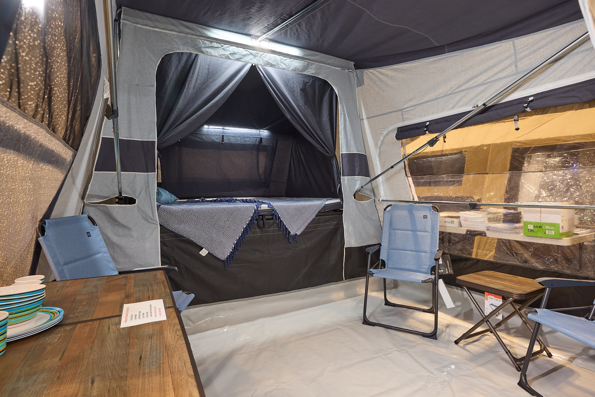 In the Jamet Compact Eco there are three blue chairs, a table and a coffee table.  The bedroom door is open.  There is lighting on the ceiling.