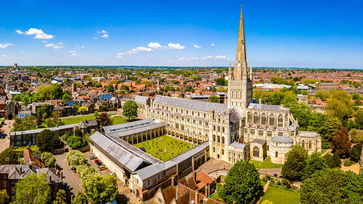 An aerial view of Norwich Cathedral showing the dramatic spire rising into the blue sky