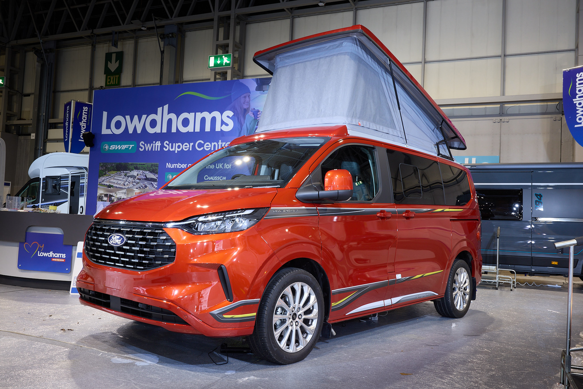 The Swift Monza is orange, its pop top roof is open and the canvas is pale blue.