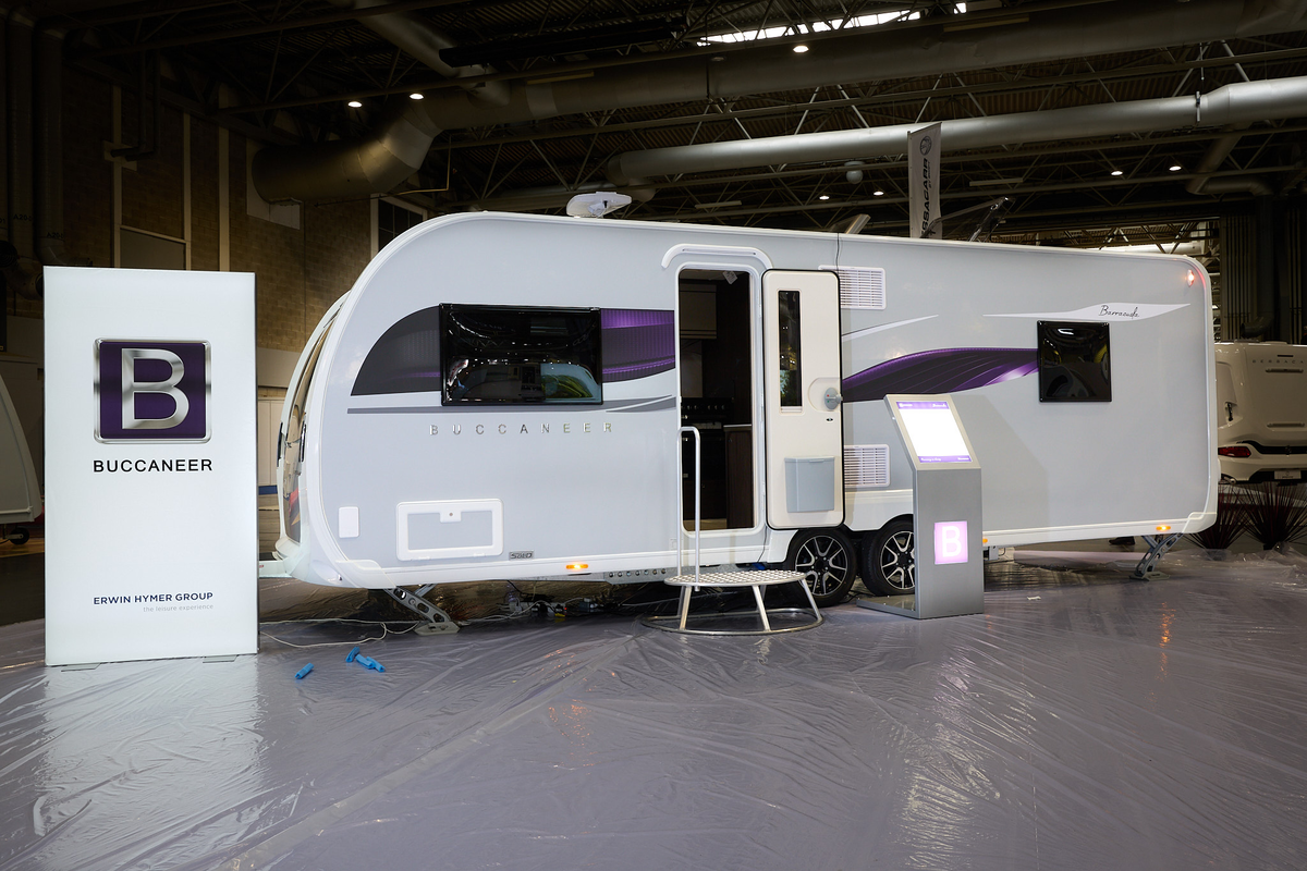 Buccaneer Barracuda exterior’s grey with purple decals.  The entrance door is open and there is a fixed metal step into its interior.  There is an interactive stand next to the steps.