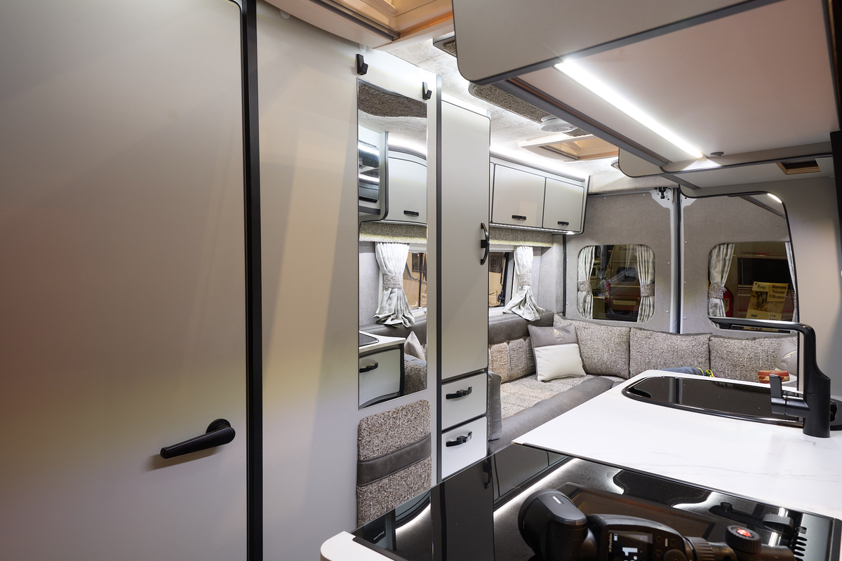 The Aura Campervans 7 EL has a rear lounge.  The upholstery is pale and dark brown.  The cabinets are cream.  There is a hob in the front.  