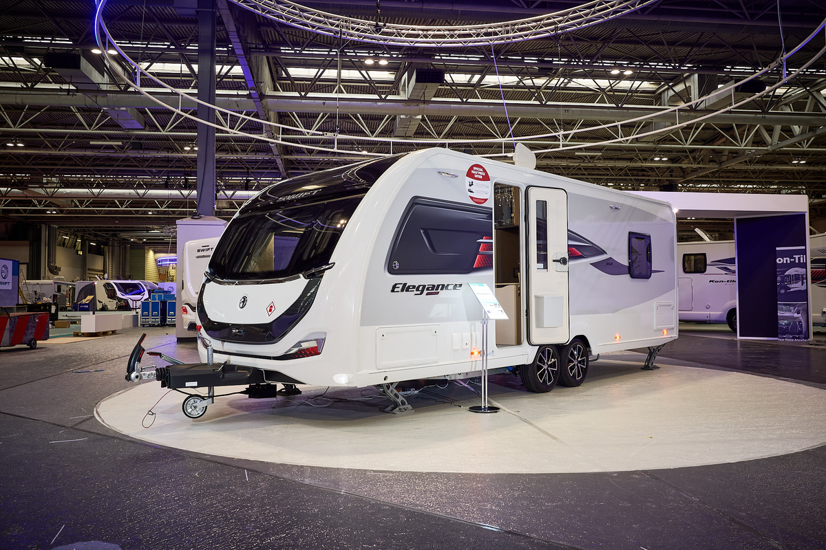 Swift Elegance Grande 860's exterior is white and grey with a large front window.  There are black graphics on the front panel.  The door is open and its corner steadies are down.  It has a twin axle. 