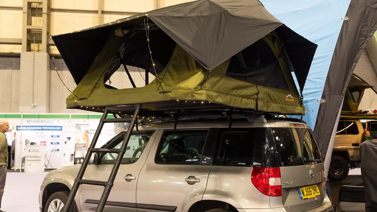 The Escapade 4x4 Summit has a two tone green canvas.  It has a black ladder to gain access.  It is displayed on a bronze car.