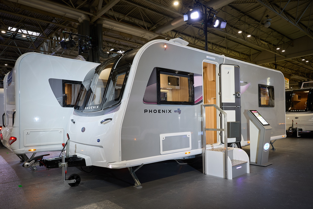 Bailey Phoenix 640 exterior’s, grey and white with a large single front window.  The entrance door is open and there are fixed metal steps into its interior.  There is an interactive stand next to the steps.