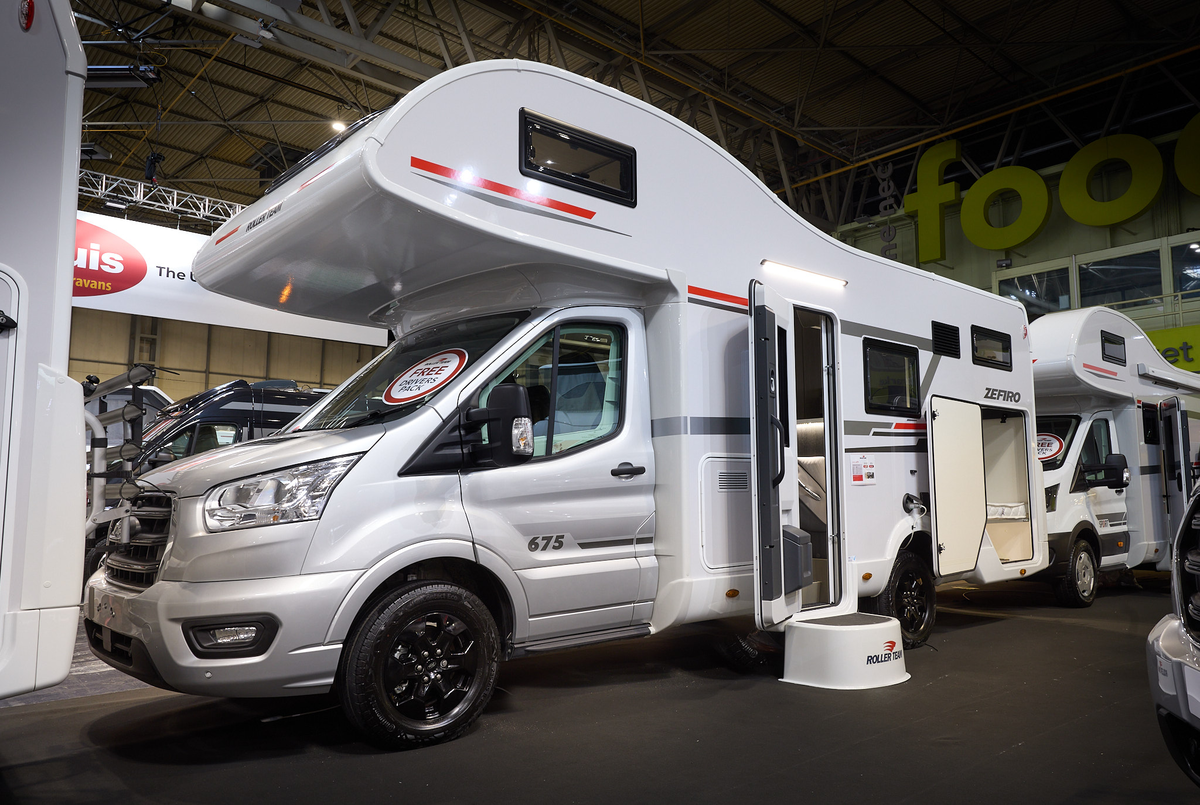 The Roller Team Zefiro 675 has a silver cab and its body is white with grey and red decals.  There is a white step outside the open habitation door.  The rear locker door is open.