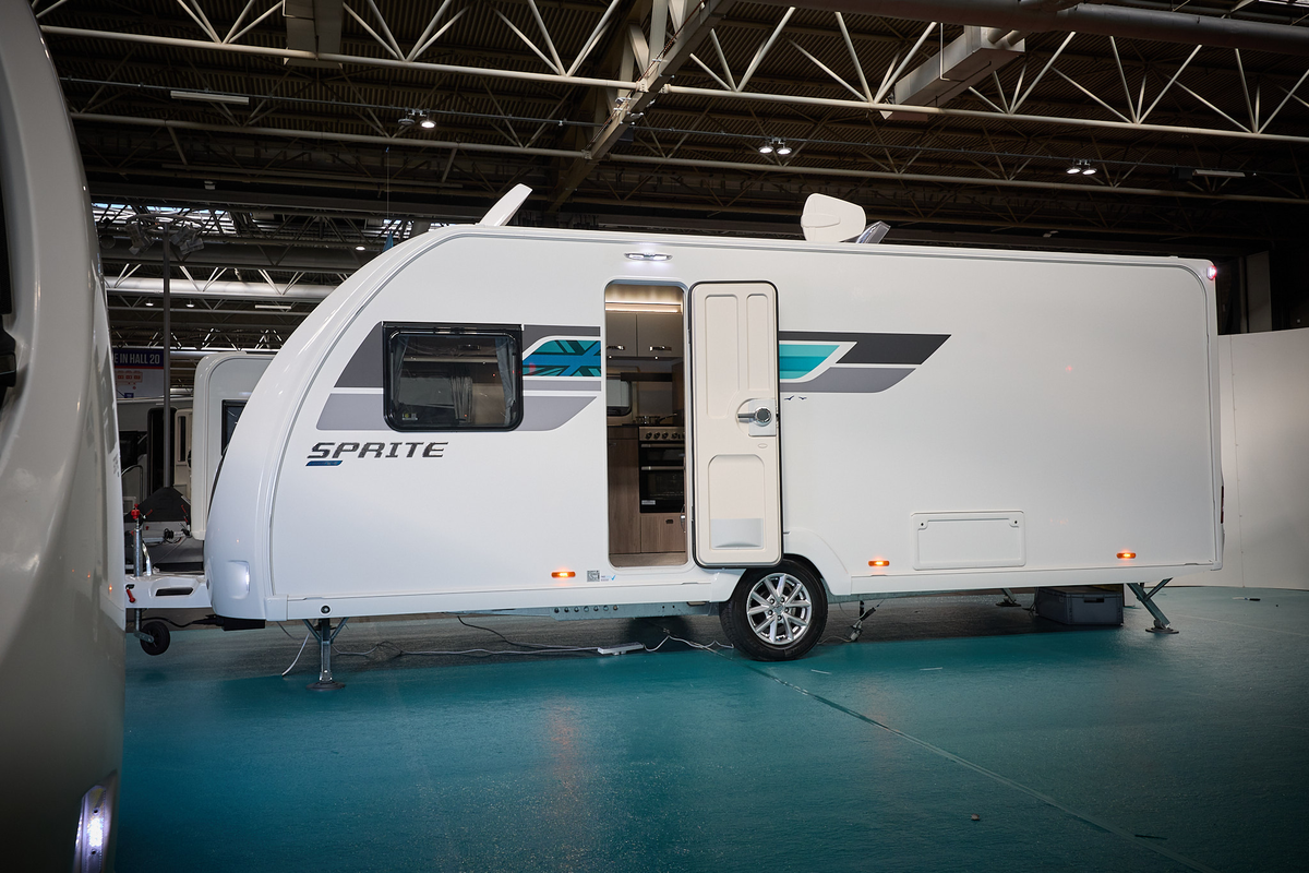 Swift Sprite Grande Quattro FB has a white exterior with grey and turquoise graphics.  It's door and skylight are open.  It has a single axle.