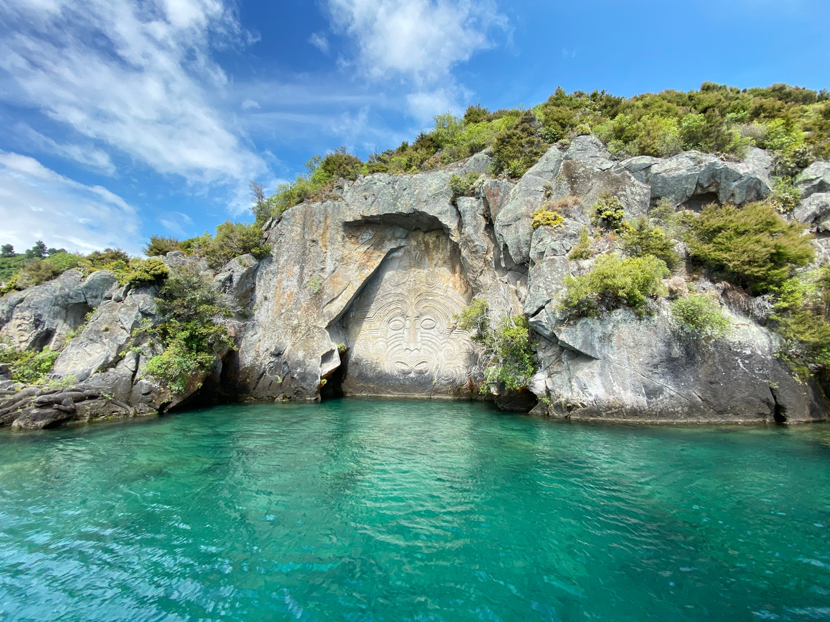 Turquoise water leading up to a rock face with carvings 